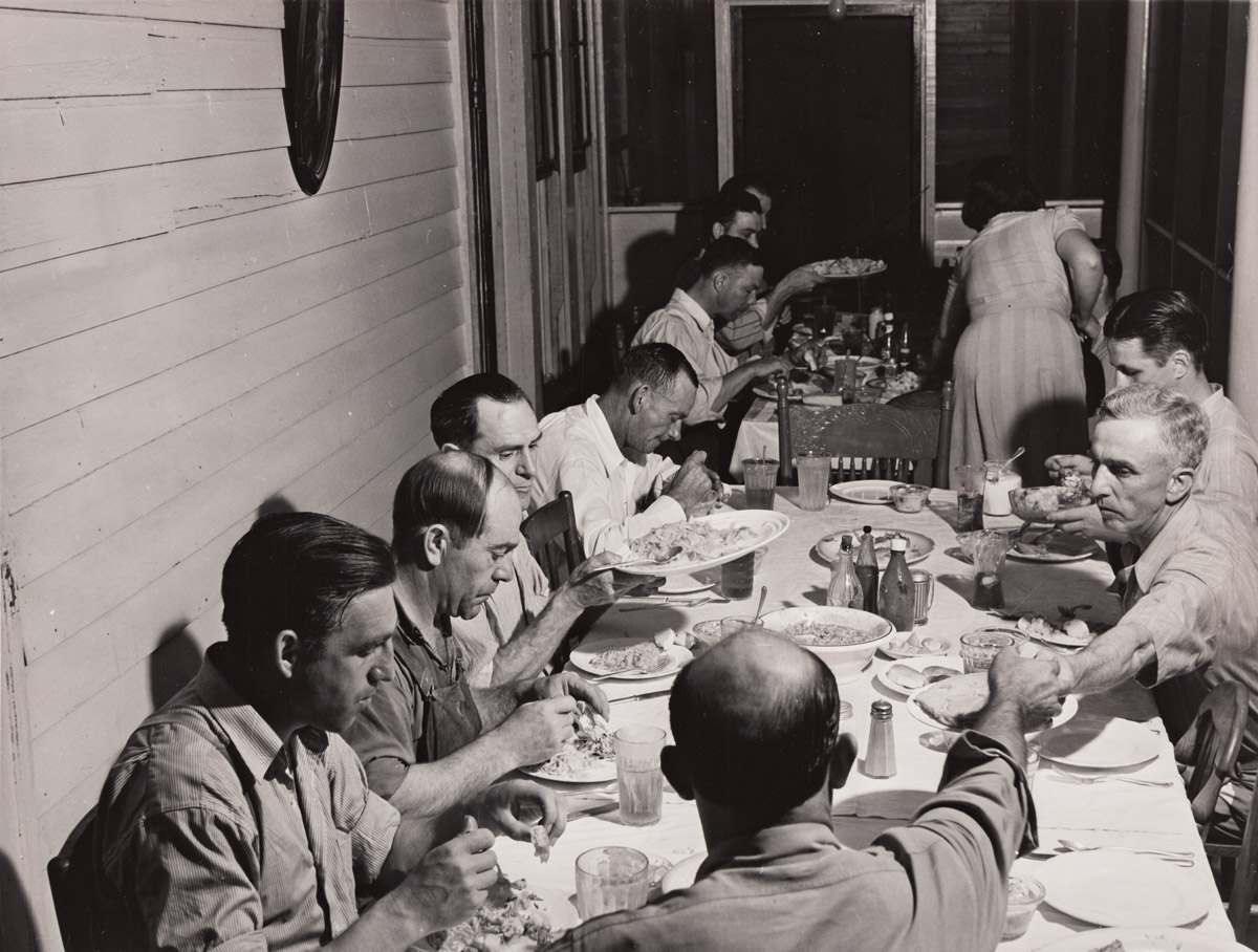 JACK DELANO (1914-1997) Man speaking to group * Workers from the nearby powder plant having dinner at their boarding house in Childersb